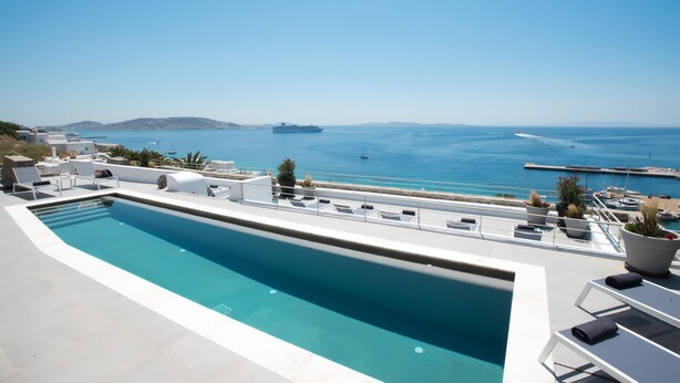 Piscina no terraço com vista para o mar e um navio ao longe.