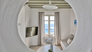 Uma sala de estar moderna com uma mesa redonda, uma poltrona confortável, televisão fixada na parede e vista para o mar através de grandes janelas.