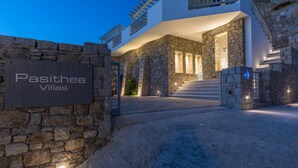Entrada com paredes de pedra para Pasithea Villas, com uma placa, uma escadaria e uma estrutura de edifício moderna.