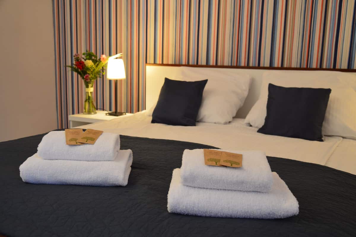 Habitación de hotel con cama, dos almohadas, mesita de noche con lámpara y un jarrón de flores.