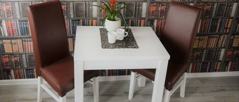A white table with two brown chairs, a potted plant, and a tray with a mug and a cup.