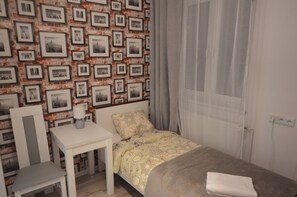 Un dormitorio con cama, una silla, una mesita y una pared decorada con marcos.
