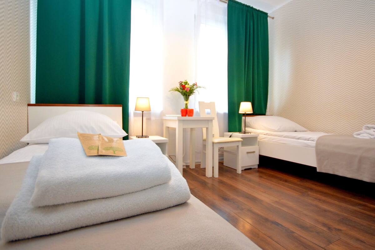 Una habitación de hotel con dos camas, una mesita, una silla y una mesita de noche con lámparas.