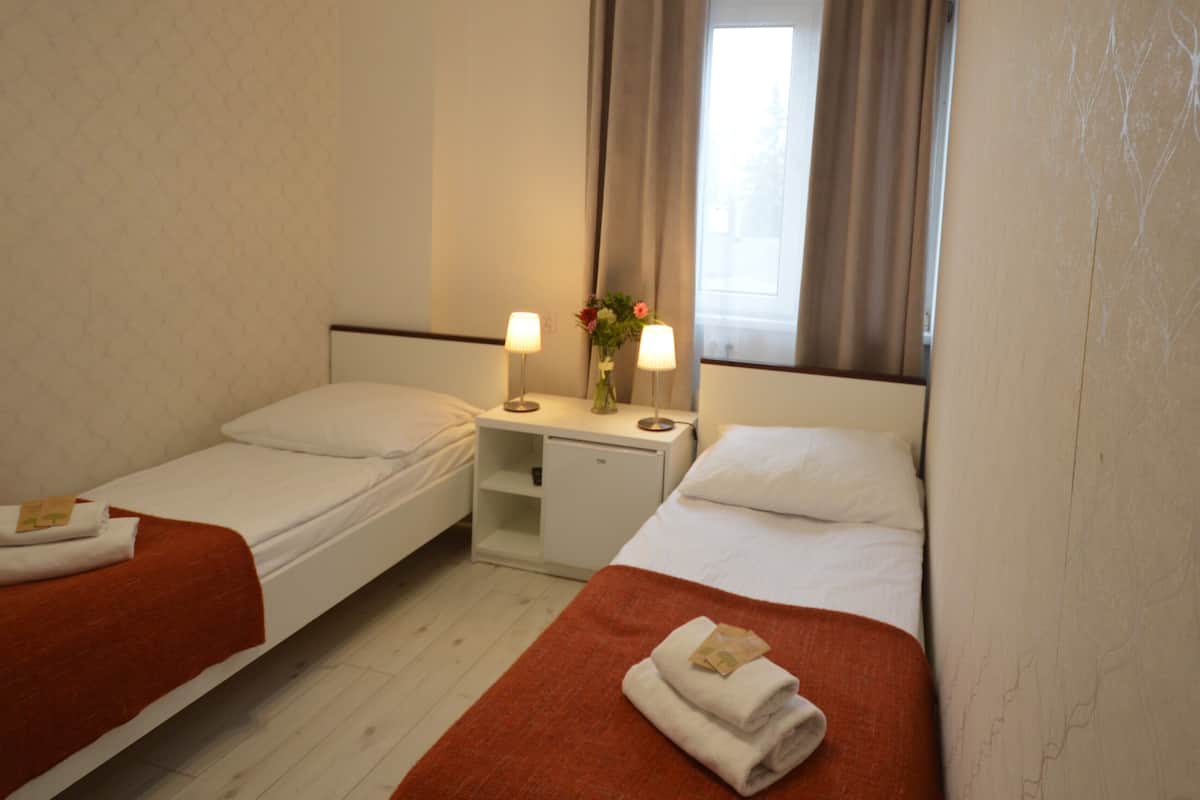 Habitación doble con dos camas individuales, un escritorio pequeño con lámpara y una ventana con cortinas.