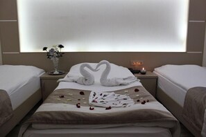 A hotel room with two beds, a vase with flowers, a clock, and a heart-shaped towel arrangement on the bed. - Derya Otel (Konya)
