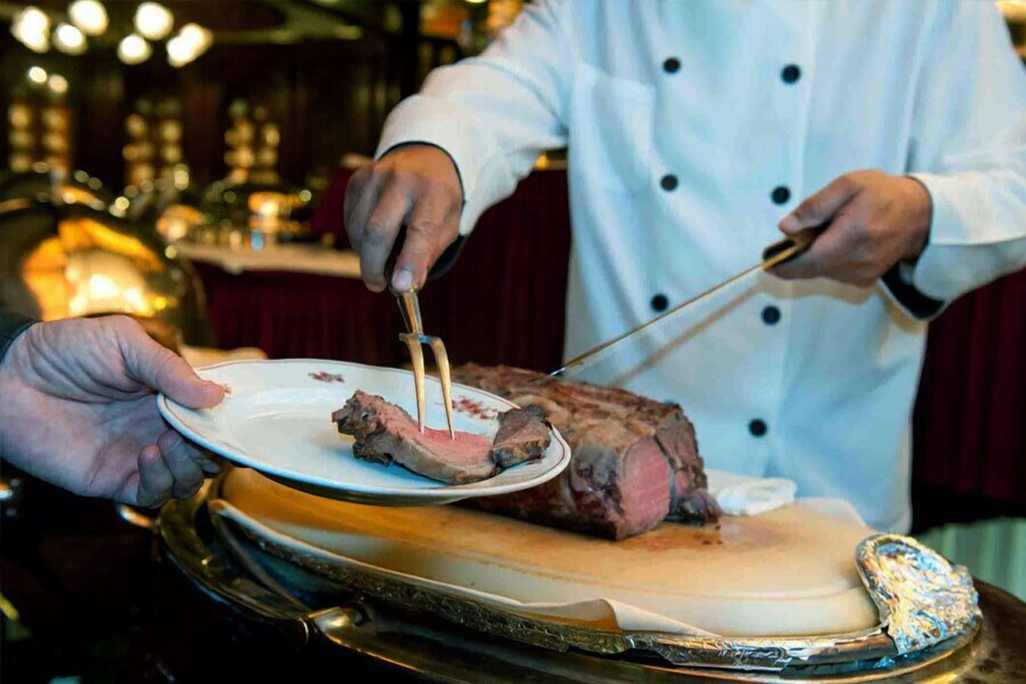 Un chef corta una porción de carne en un plato.