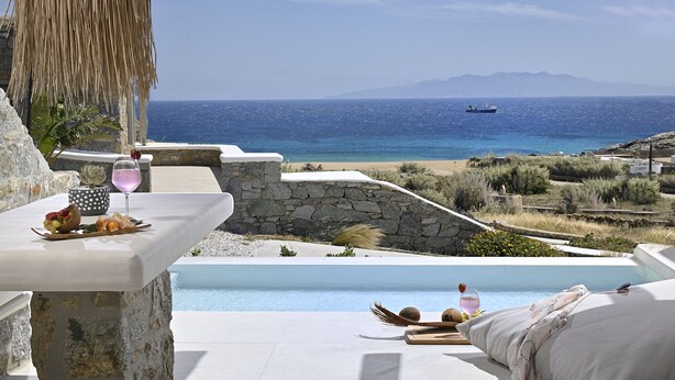 A terrace with a pool, stone walls, and a view of the sea and mountains. - VLIA Myconian Residences (Mykonos)