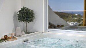 A bathtub with a view of the sea, a small tree, and some towels and fruit. - VLIA Myconian Residences (Mykonos)