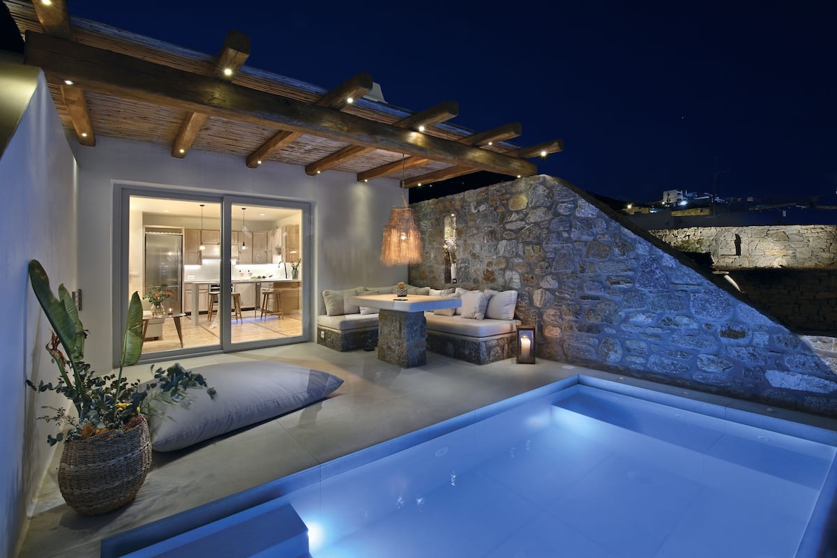 A modern outdoor living area with a stone wall, a pool, and a cozy seating area with cushions.