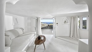 A minimalist room with a bed, a small table, and a view of the sea. - VLIA Myconian Residences (Mykonos)