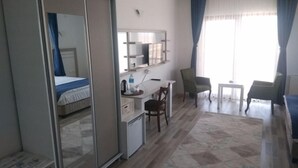 Habitación de hotel con cama, escritorio, silla, armario y ventana con cortinas.