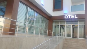 Entrada de hotel con fachada de vidrio, una escalera de metal y un letrero que dice "OTEL".