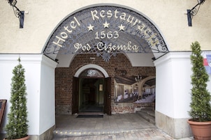 A entrada do Hotel Restaurante 1563 Pod Ciemka, com fachada de tijolos e um arco de metal decorativo.