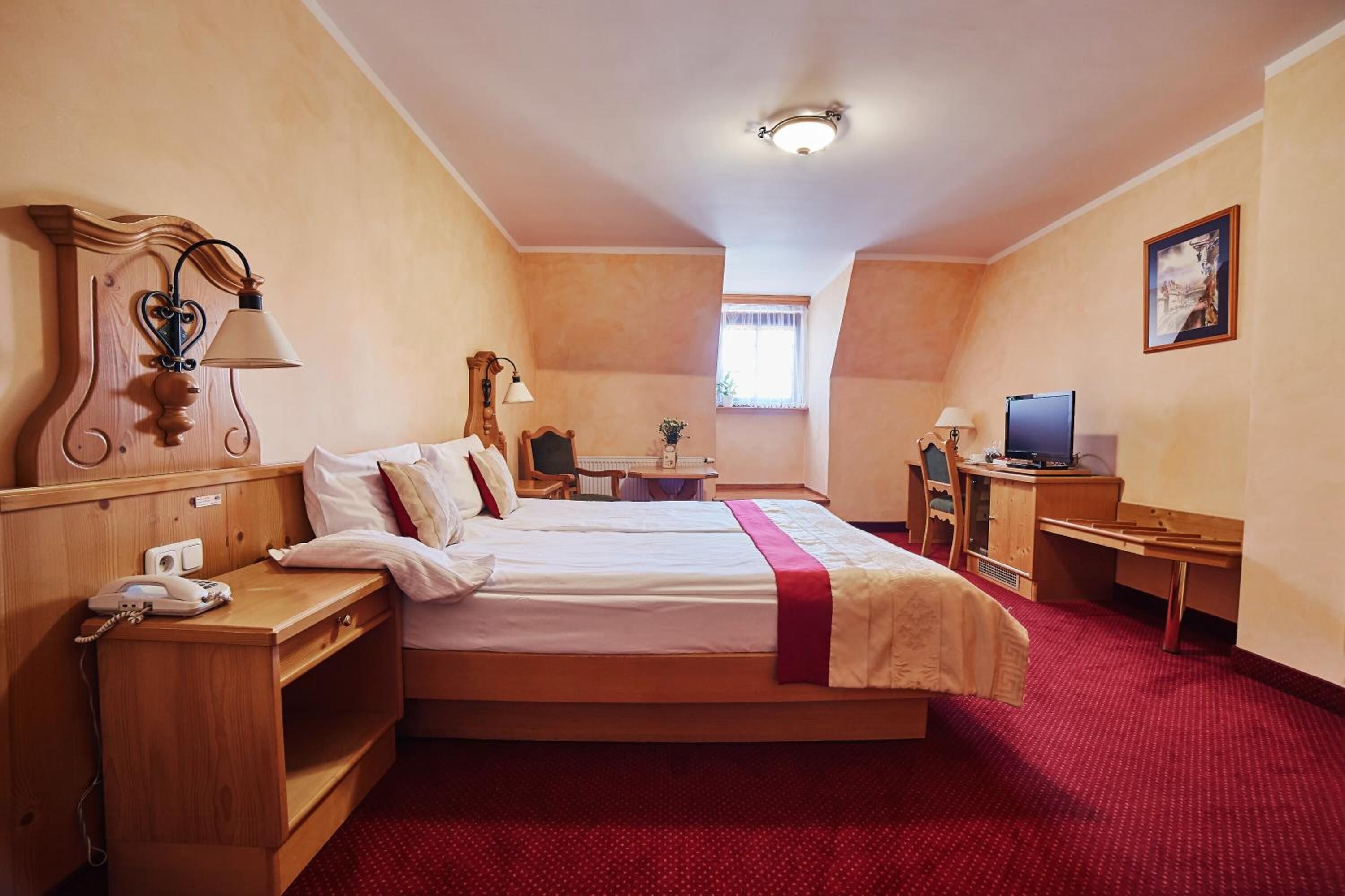 A hotel room with a bed, bedside table, lamp, desk, chair, and a television.