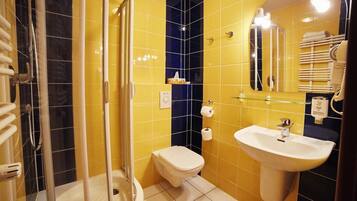 Een badkamer met gele en zwarte tegels, een glazen douchecabine, een wit toilet en een wastafel met een spiegel erboven.