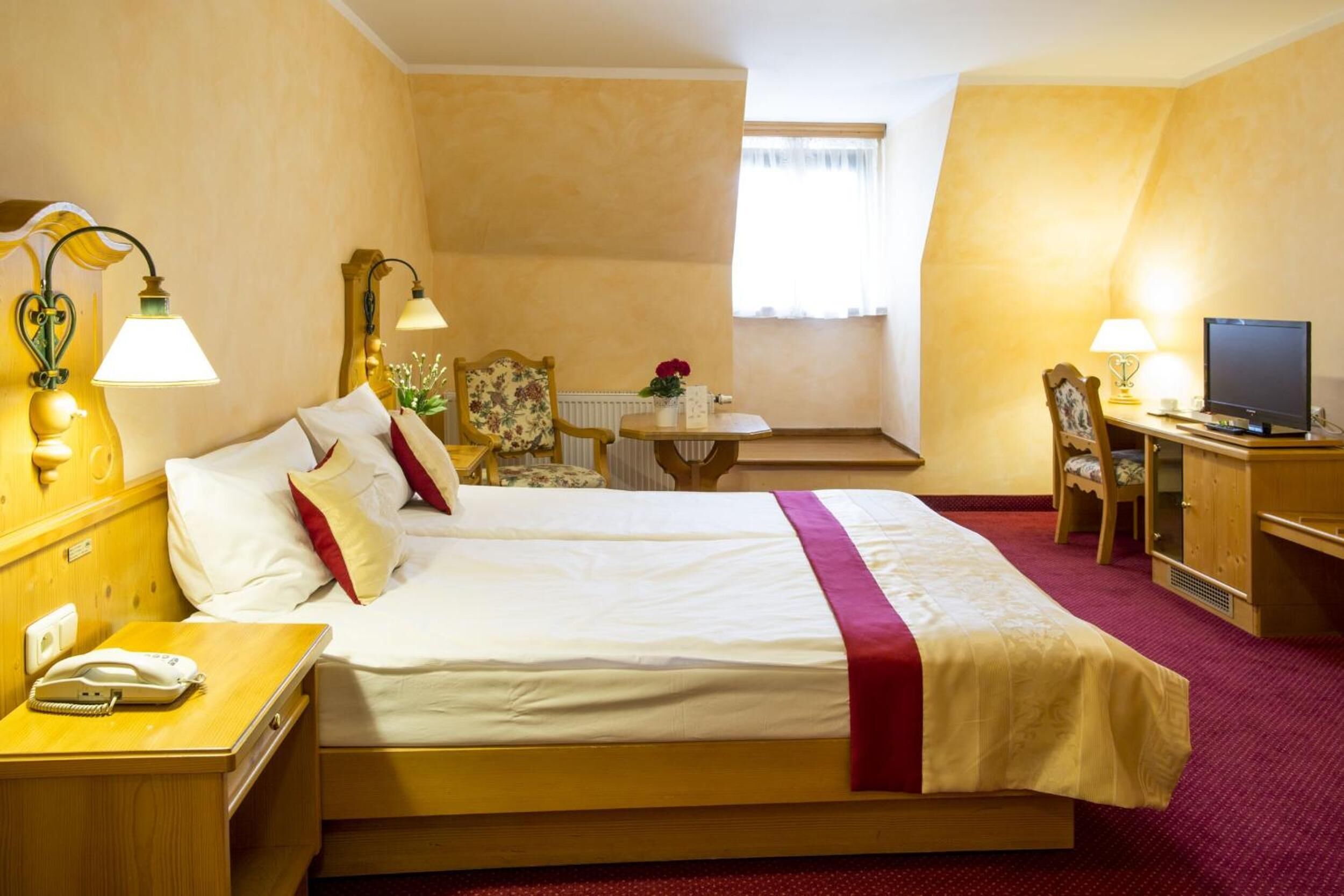 Une chambre d’hôtel avec un grand lit, des lampes de chevet, un bureau avec un ordinateur, une chaise et une petite table sur laquelle est posé un vase avec des fleurs.