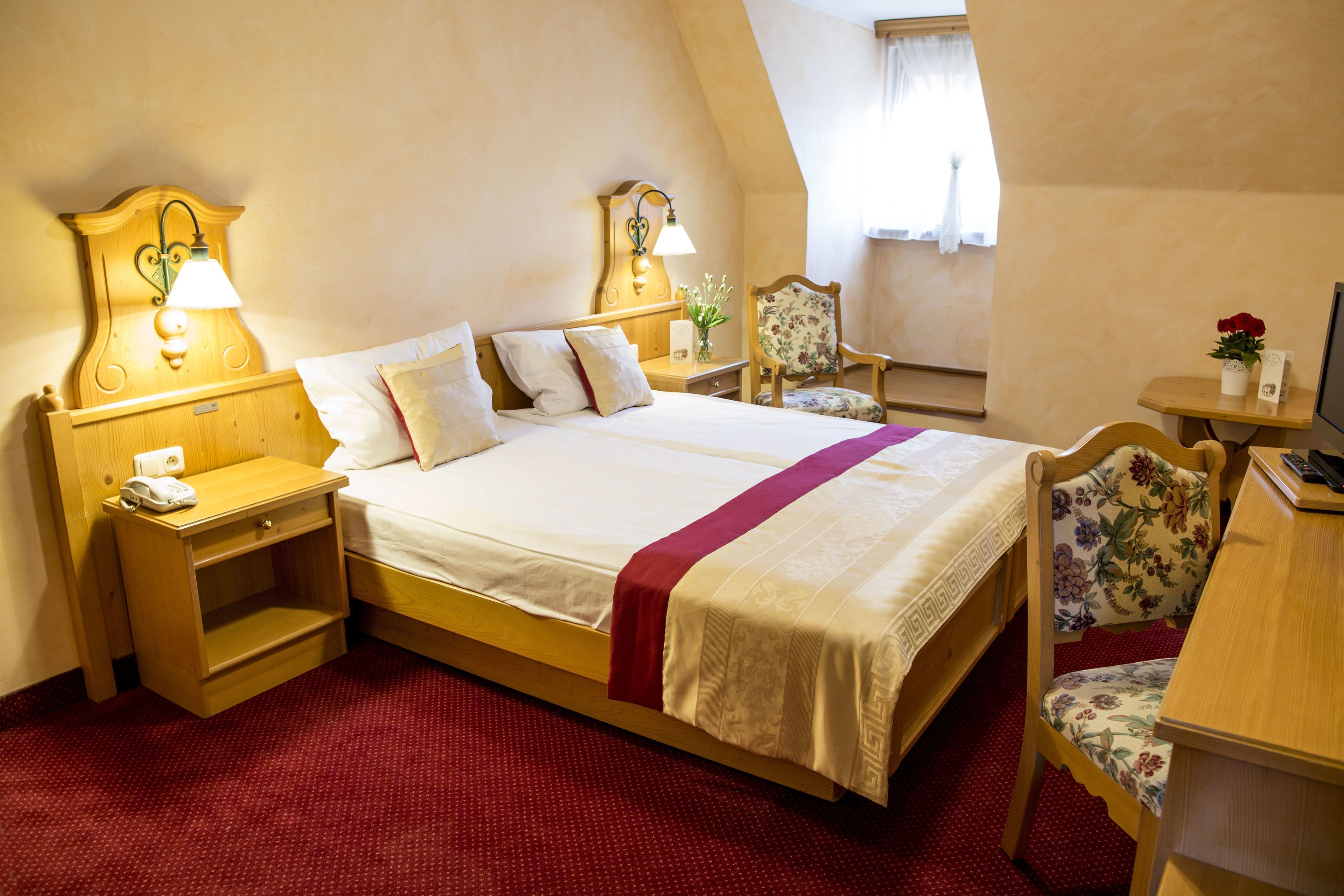 A hotel room with a bed, bedside tables, a desk, and a chair.
