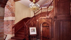 A grand staircase with a wooden handrail and a chandelier, leading to a door with a decorative iron gate. - Hotel pod Cizemka (Sandomierz)