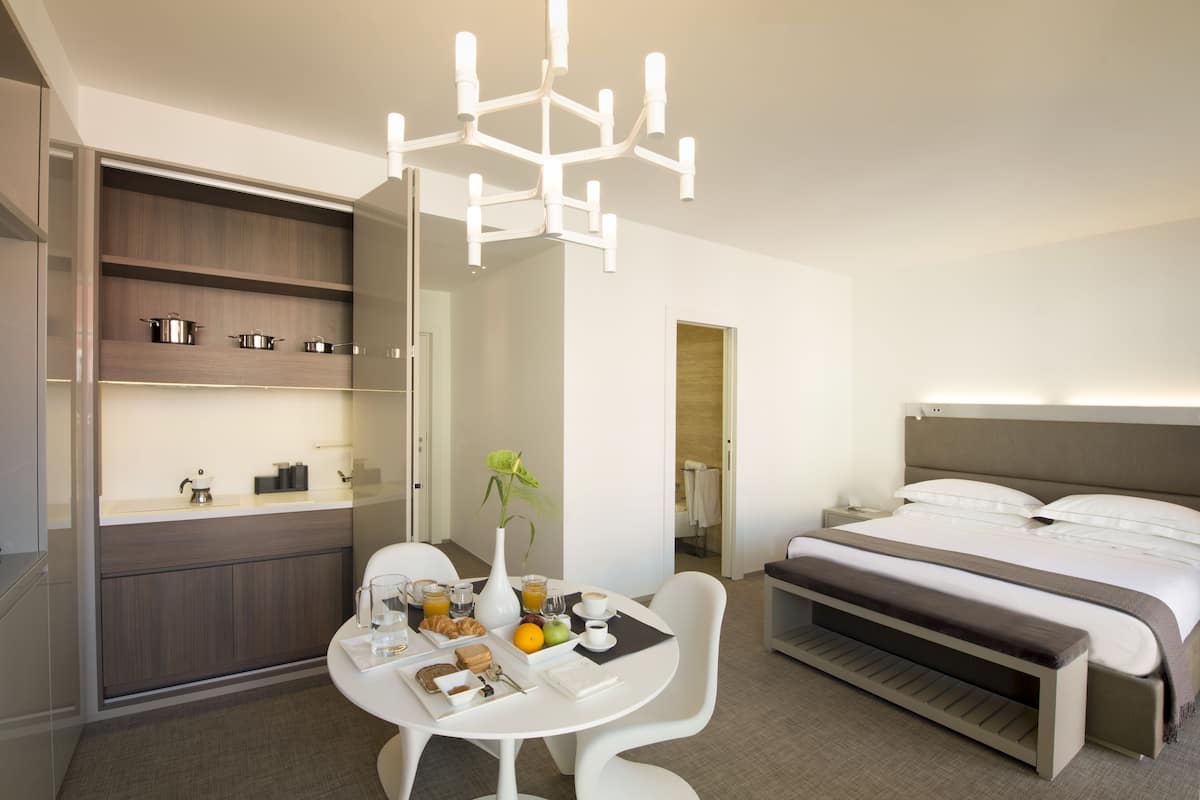 A modern hotel room with a dining area, a bed, and a built-in wardrobe.