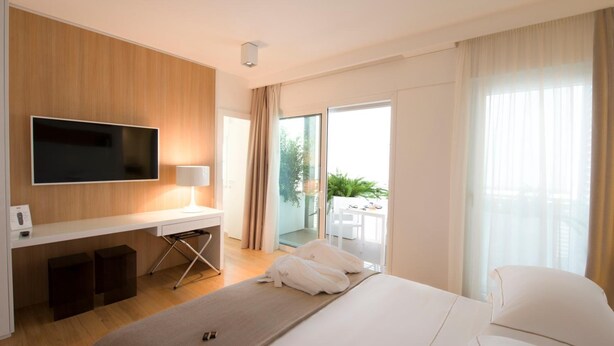 A modern hotel room with a large bed, a flat-screen TV mounted on a wooden wall, a desk with a lamp, and a sliding glass door leading to an outdoor area. - Dilman Luxury Stay (Bari)