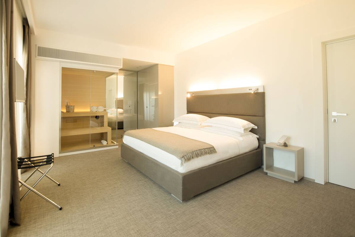A modern hotel room with a large bed, a bedside table, a wardrobe, and a mirror.