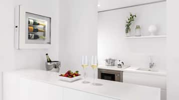 A modern kitchen with a white countertop, a wine cooler, a bowl of strawberries, and two glasses of white wine.