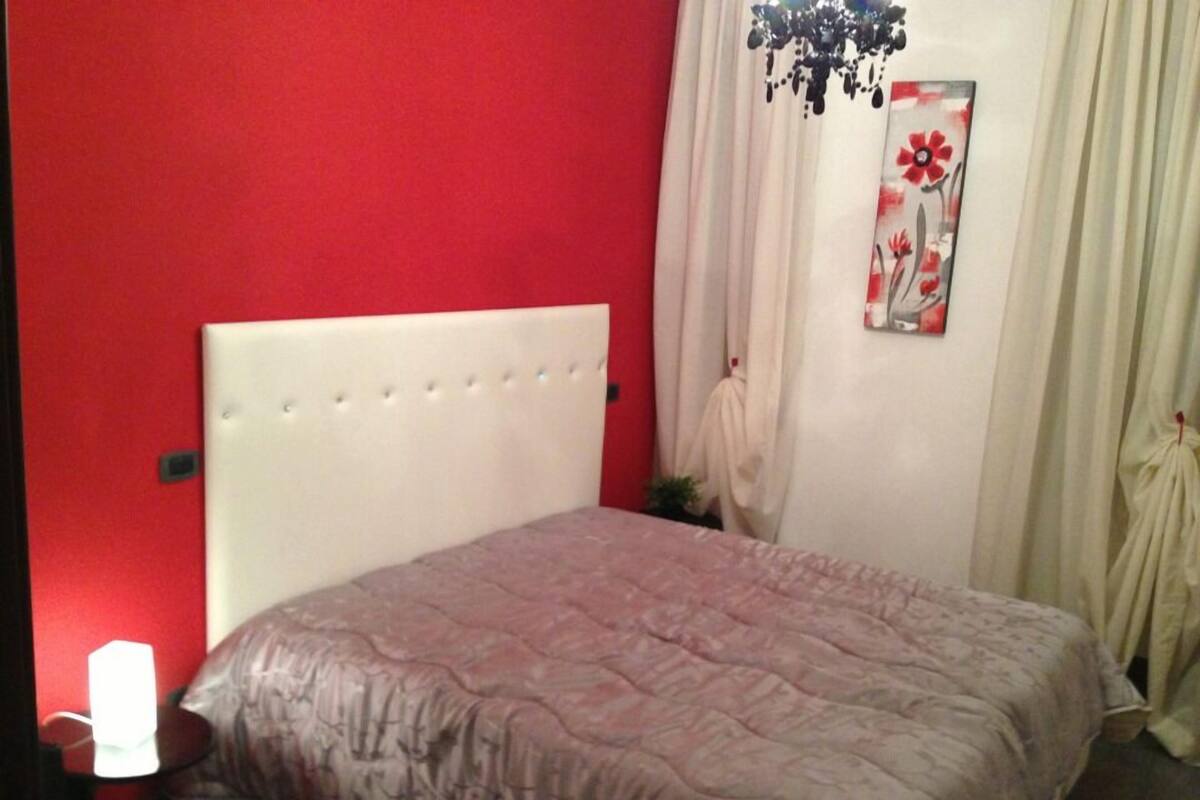 A bedroom with a red wall, a white headboard, and a bed with a patterned bedspread.