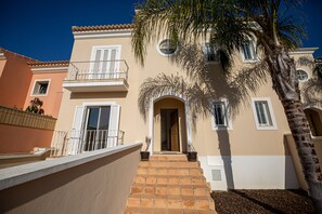 Un immeuble à plusieurs étages doté d’un balcon, d’une porte et d’un palmier.