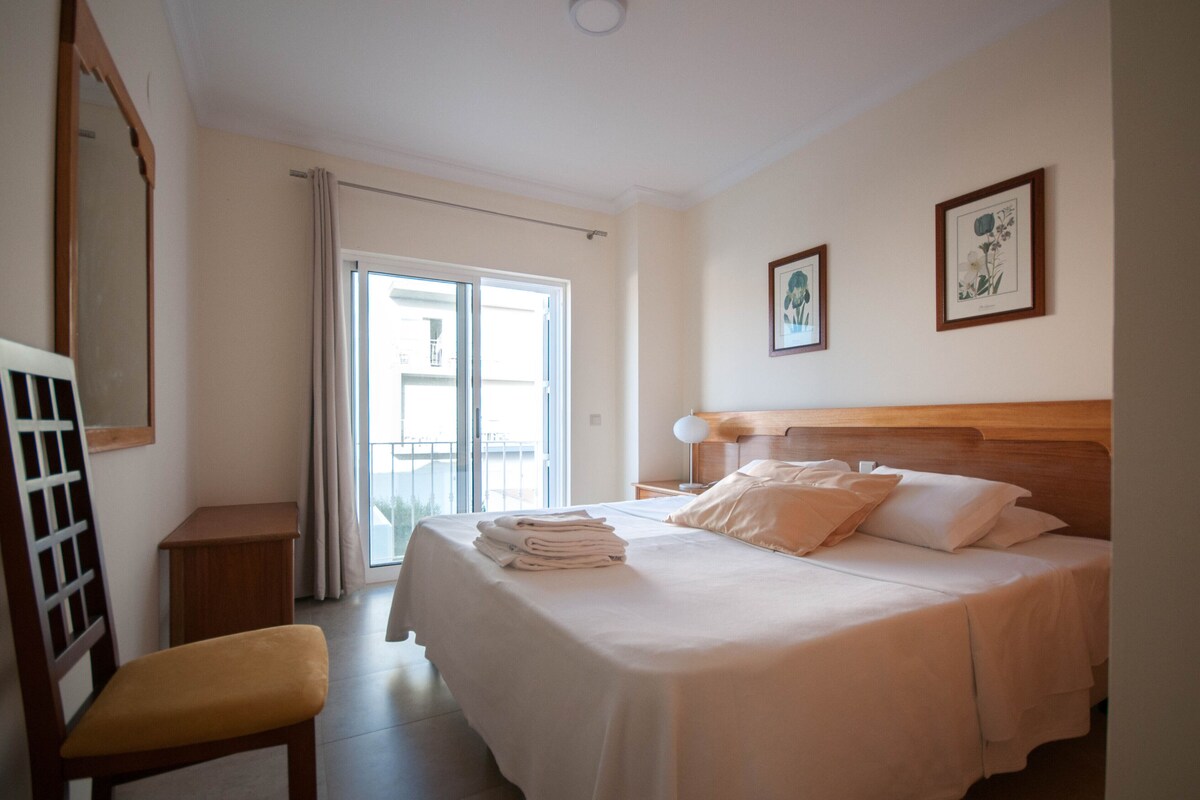 Une chambre d’hôtel avec un lit, une chaise, une table de chevet et une fenêtre avec des rideaux.