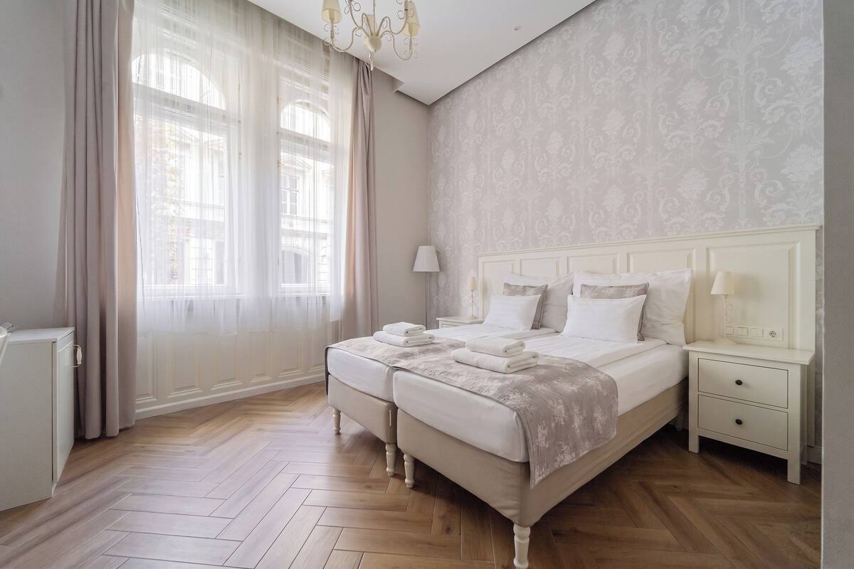 A hotel room with a large bed, two bedside tables, a nightstand, a lamp, and a wardrobe.