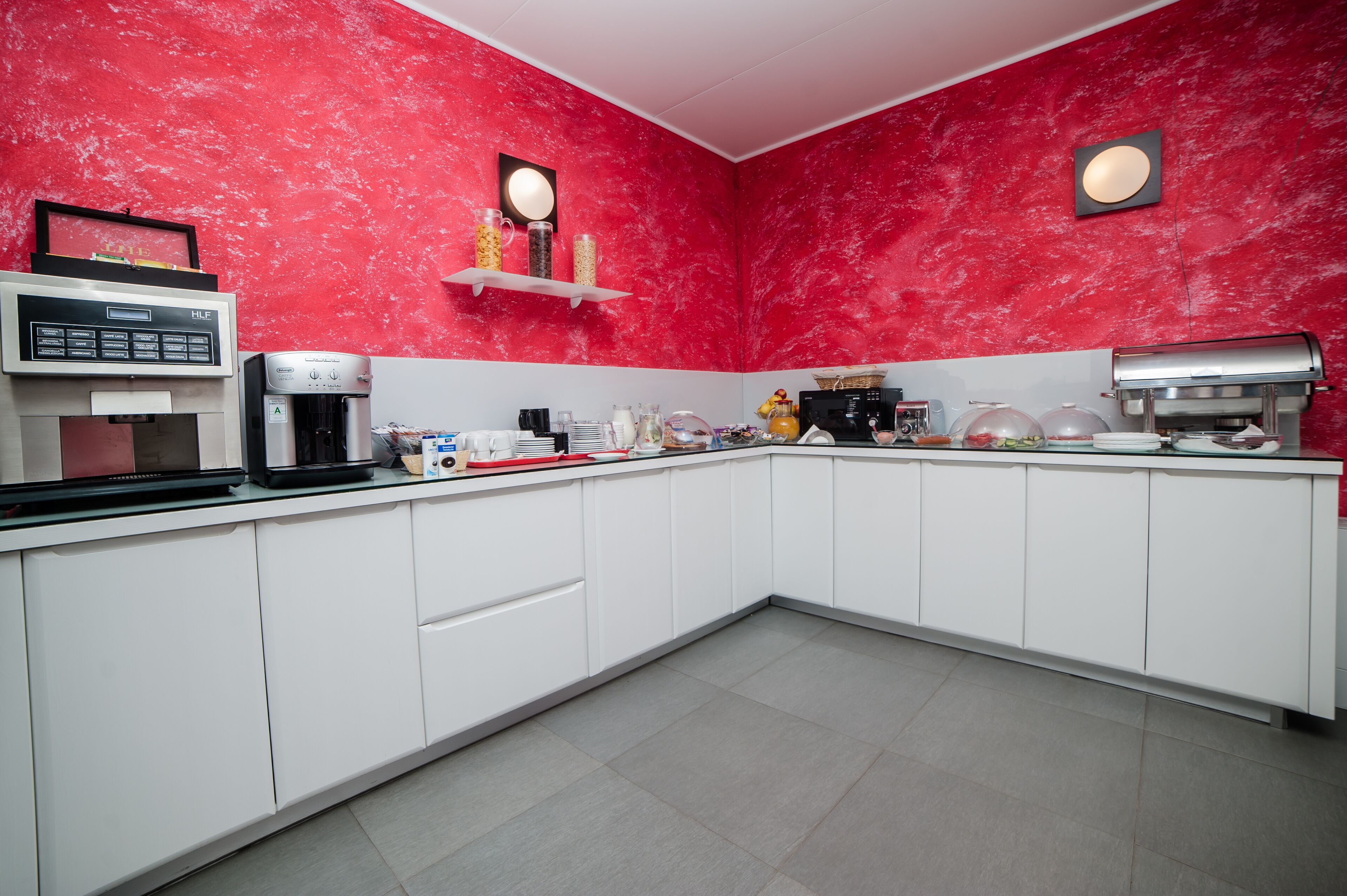 Una cocina moderna con armarios blancos, un salpicadero de mármol rojo y varios electrodomésticos como una cafetera y un microondas.