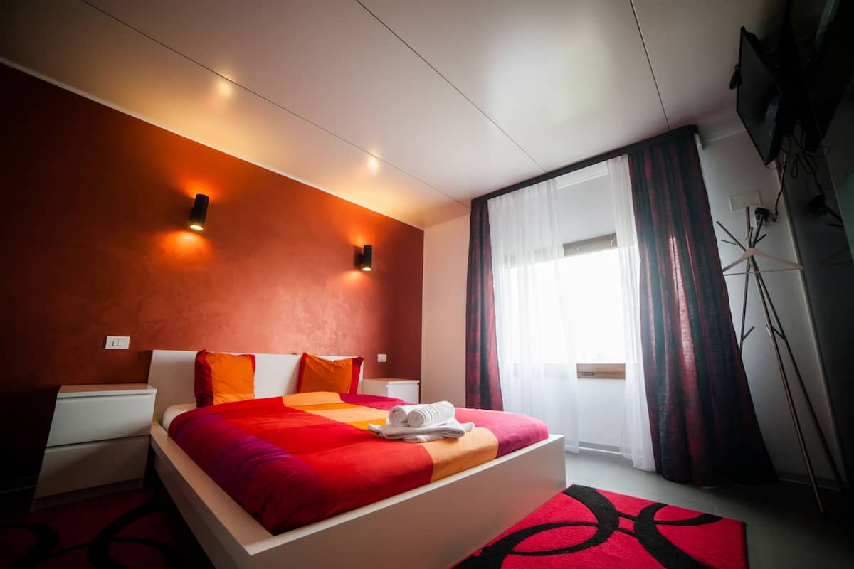 Moderni hotellihuone, jossa on suuri sänky, yöpöytä, televisio ja ikkuna, jossa on verhot.