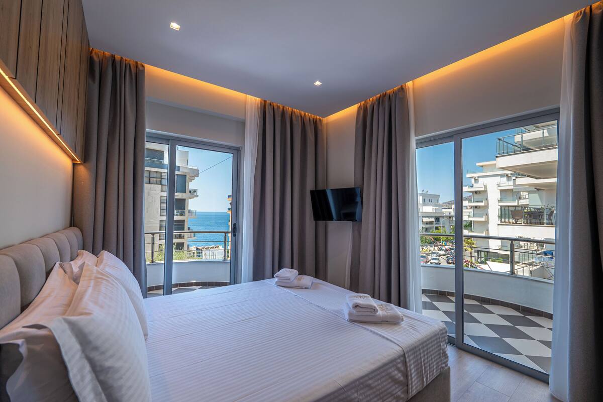 A modern hotel room with a large bed, a flat-screen TV, and a balcony with a city view.