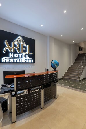 A hotel reception desk with a sign for 'AREL HOTEL RESTAURANT,' a globe, and a staircase. - Arel Hotel (Sarandë)