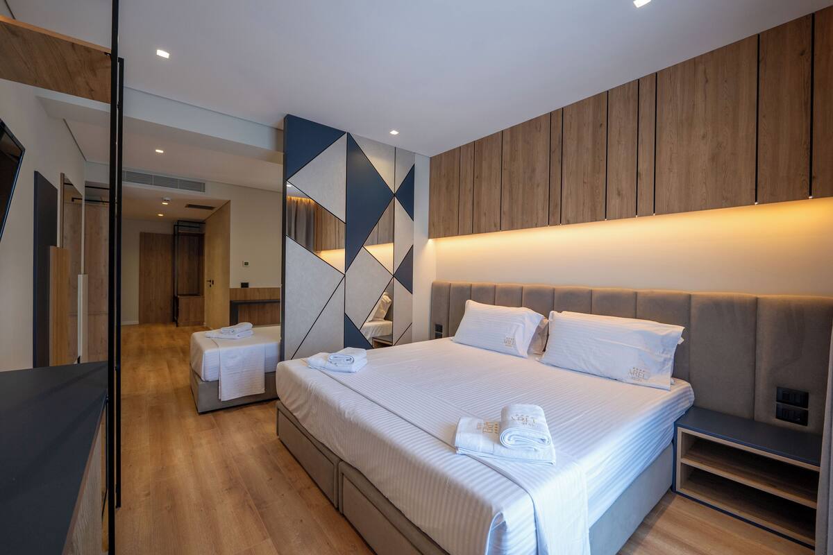A modern hotel room with a large bed, a bedside table, and a built-in bench.