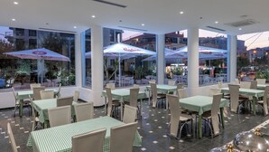 An outdoor dining area with tables and chairs, large umbrellas, and a view of the cityscape. - Arel Hotel (Sarandë)