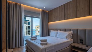 A modern hotel room with a large bed, a bedside table, and a view of the city. - Arel Hotel (Sarandë)