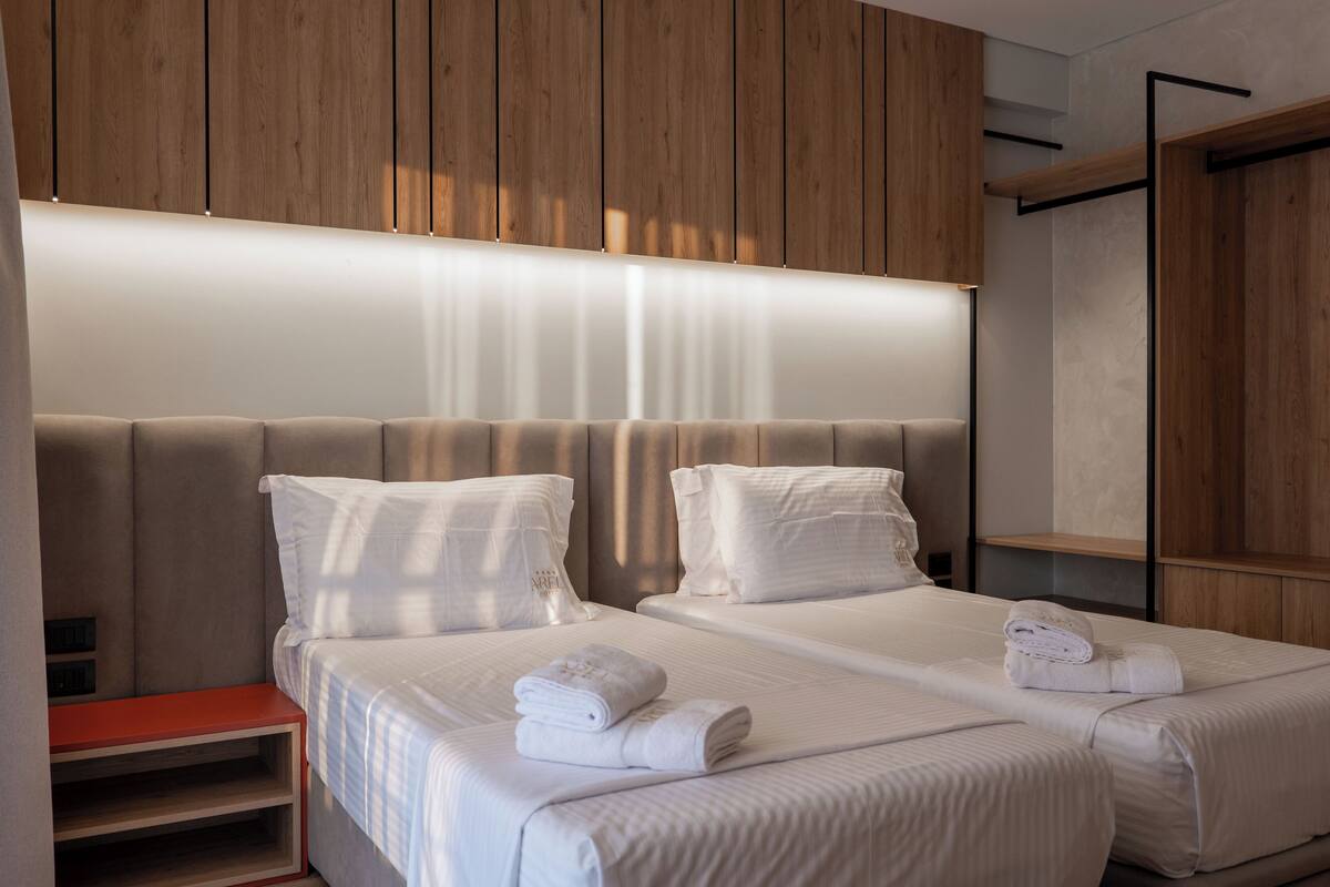 A modern hotel room with two beds, a wooden headboard, and a built-in shelf.