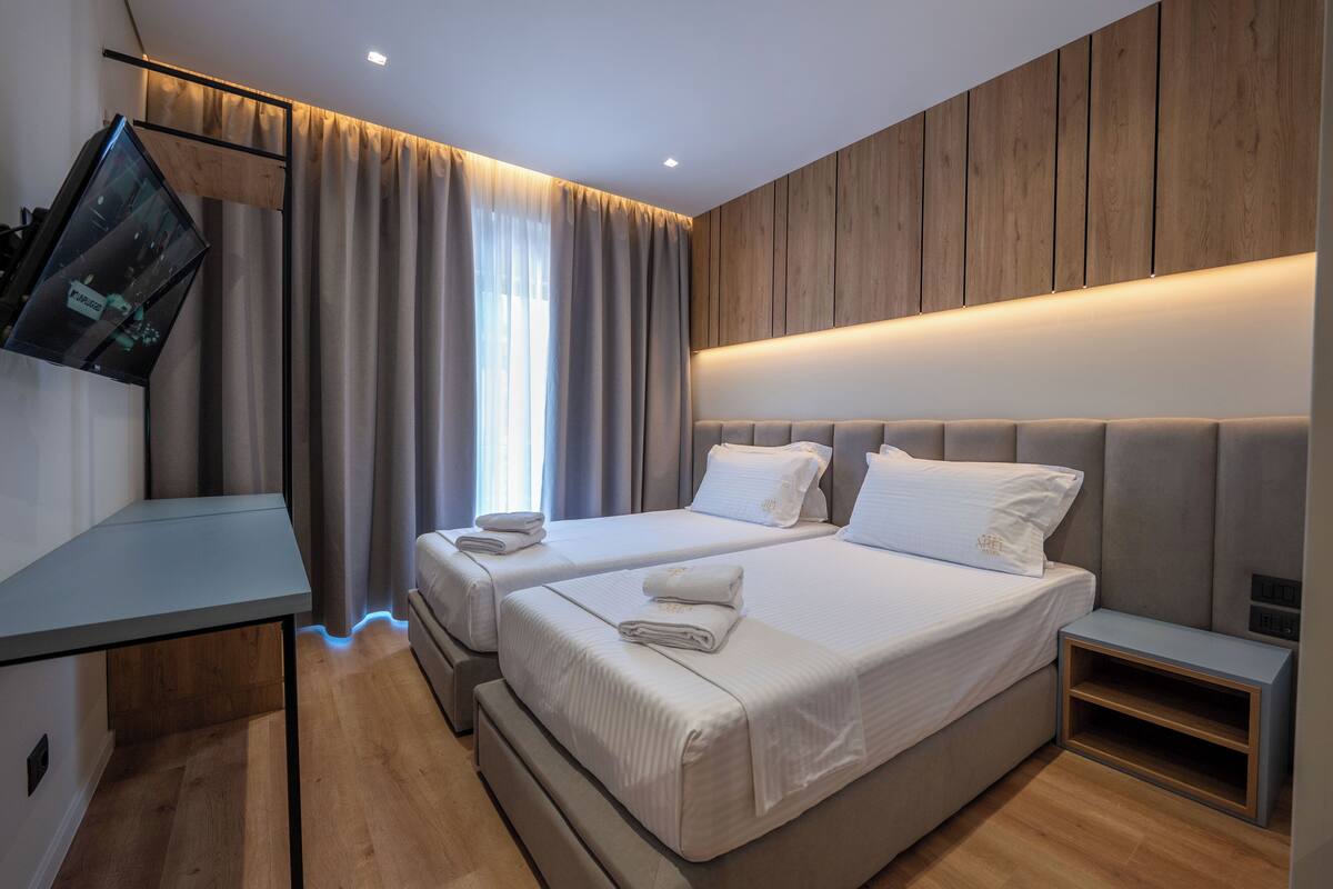A modern hotel room with two beds, a desk, and a TV.