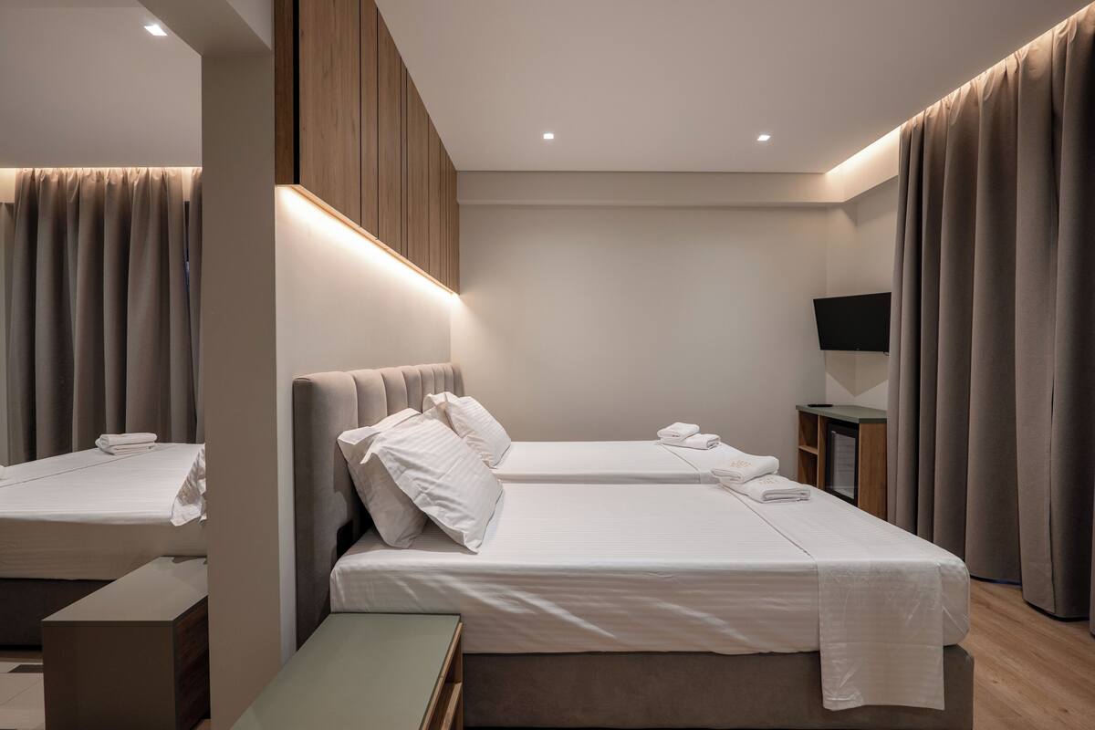 A modern hotel room with two beds, a flat-screen TV, and a wooden panel wall.