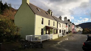 A row of traditional buildings with a stone wall and a white fence in front. - Eilean Donan View (Kyle)
