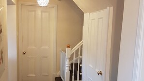 A hallway with a carpeted floor, white doors, a staircase with a white railing, and a ceiling light fixture. - Eilean Donan View (Kyle)