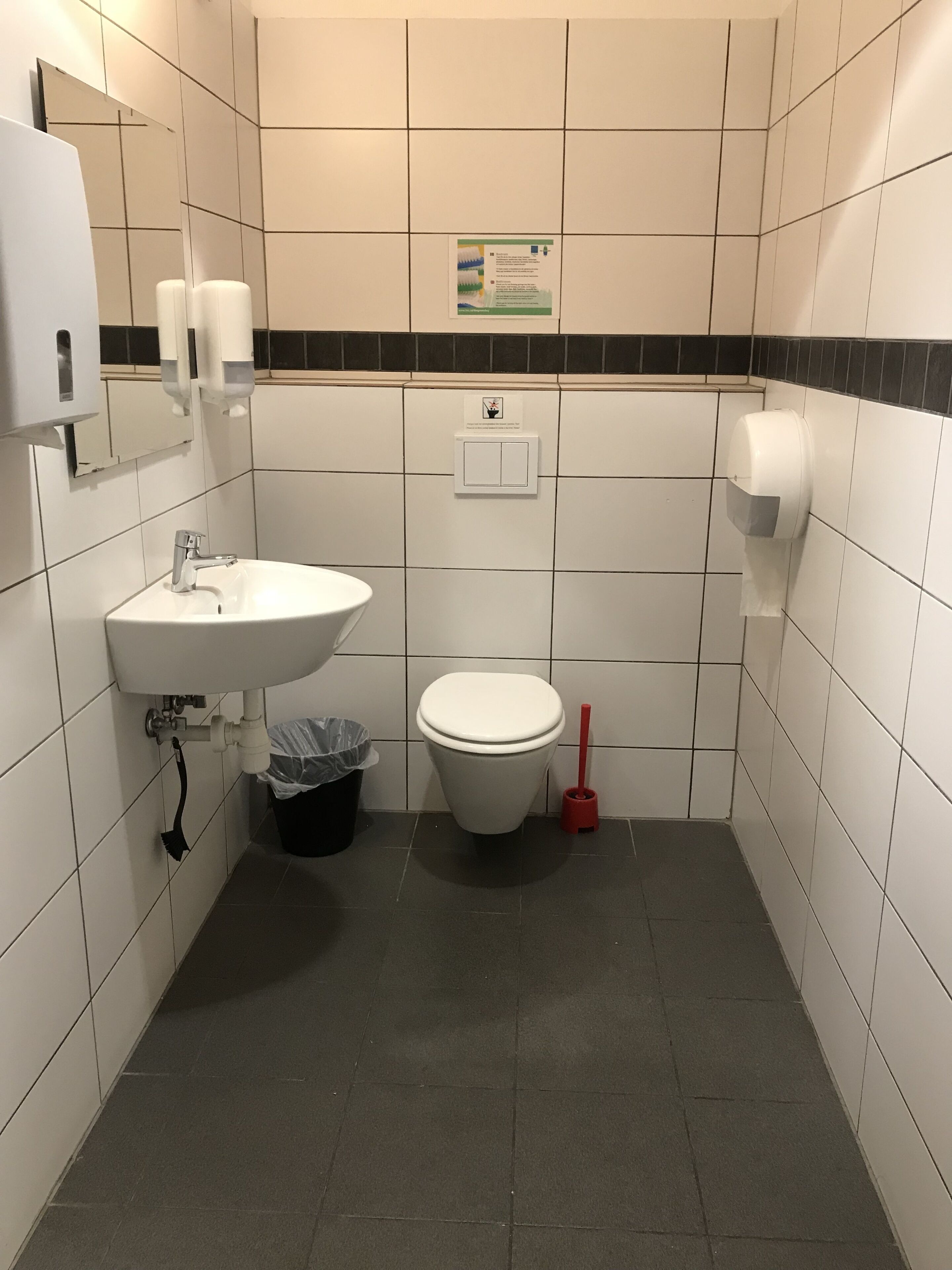 A small, tiled bathroom with a white sink, toilet, and hand dryer.
