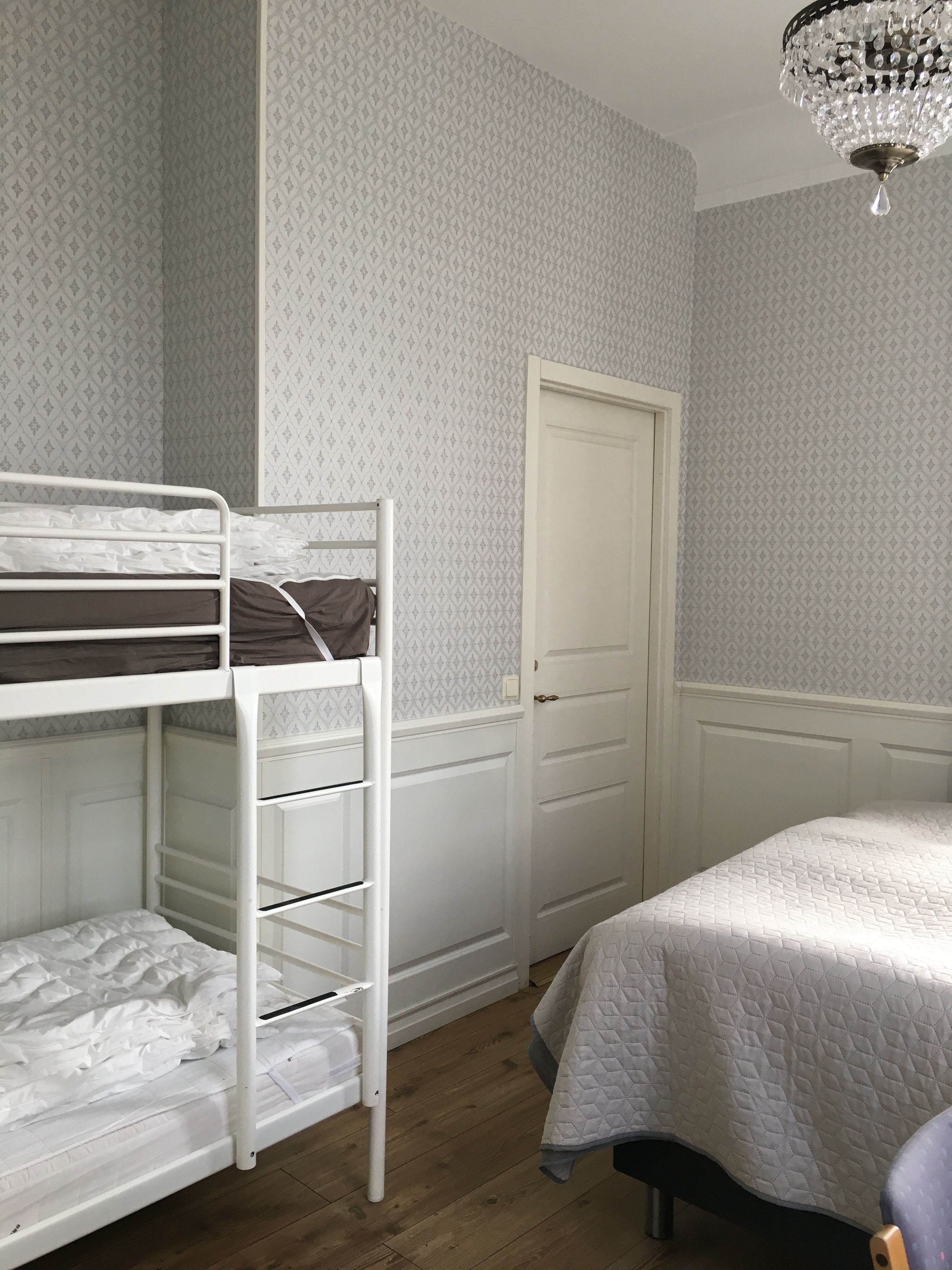 A bedroom with a bunk bed, a single bed, a door, and a chandelier.