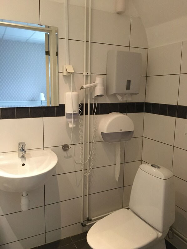 Un baño con lavamanos, inodoro y secamanos adherido a la pared.