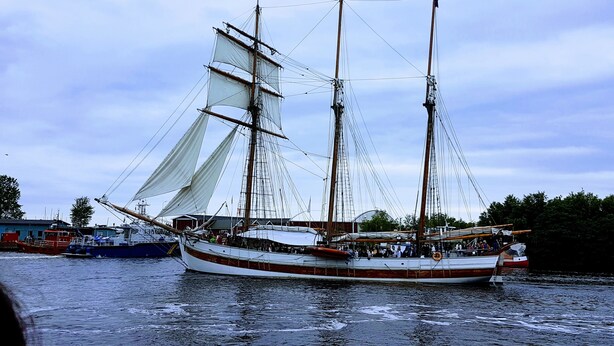 Ett stort segelfartyg med flera master och segel låg förtöjt vid en hamn.