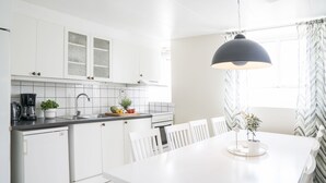 Ett modernt kök med vita skåp, en svart bänkskiva och en matplats med ett vitt bord och stolar.