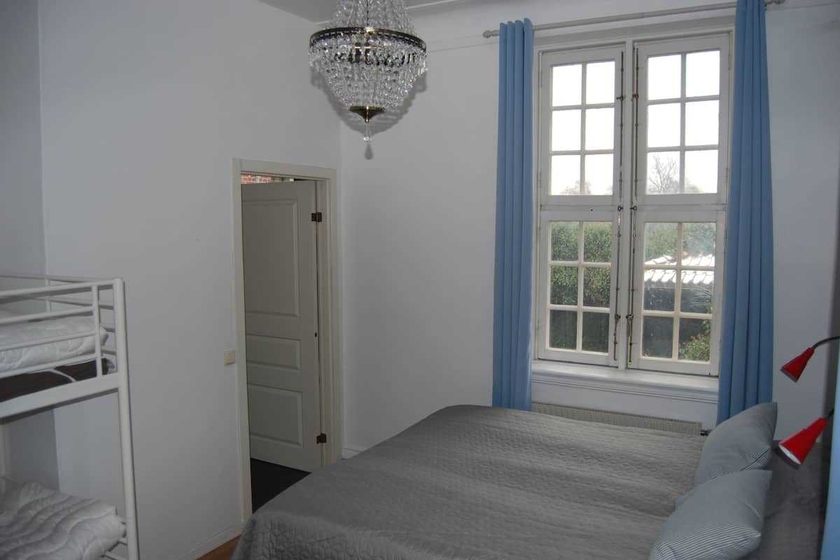 A bedroom with a bed, a chandelier, a window with curtains, and a door.