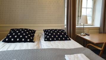 Habitación de hotel con dos camas, cada una con un cojín estampado con estrellas, un escritorio con lámpara y una ventana con cortinas.
