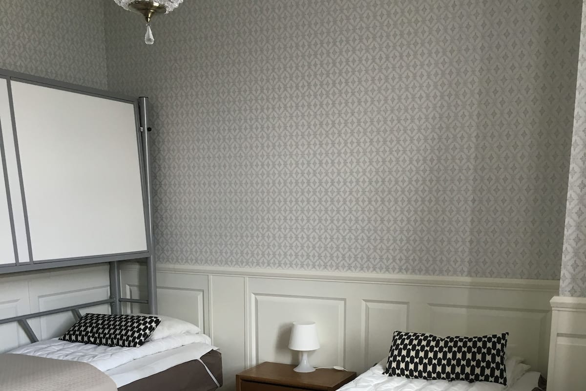 A hotel room with two beds, a nightstand with a lamp, a whiteboard, and a chandelier.